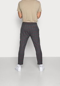 Grijze geruite broek met rode accenten, op maat gemaakt ontwerp, elastische tailleband en toelopende benen. Draag met een beige t-shirt en witte sneakers.