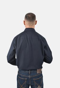 Camicia a maniche lunghe blu navy con colletto, tessuto morbido e cucitura sul retro, abbinata a jeans in denim blu con cuciture arancioni.