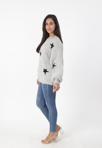 Lichtgrijze gebreide trui met zwarte sterrenpatronen, met losse mouwen. Gecombineerd met blauwe skinny jeans en doorzichtige hakken.