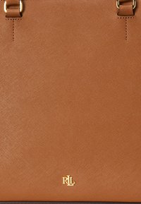 Rjava teksturirana torba z zlatimi dodatki in logotipom. Ima dvojna ročaja in strukturirano obliko. Zaključek iz saffiano usnja.