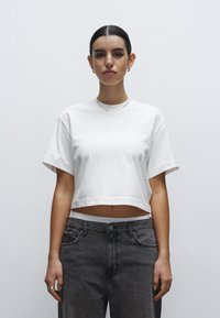 Camiseta corta blanca hecha de algodón suave con mangas cortas. Combinada con vaqueros grises descoloridos de cintura alta. Diseño simple y minimalista.