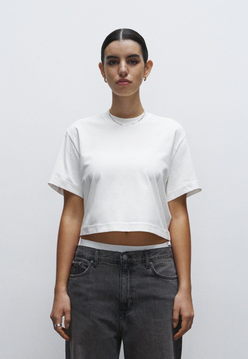 Camiseta corta blanca hecha de algodón suave con mangas cortas. Combinada con vaqueros grises descoloridos de cintura alta. Diseño simple y minimalista.