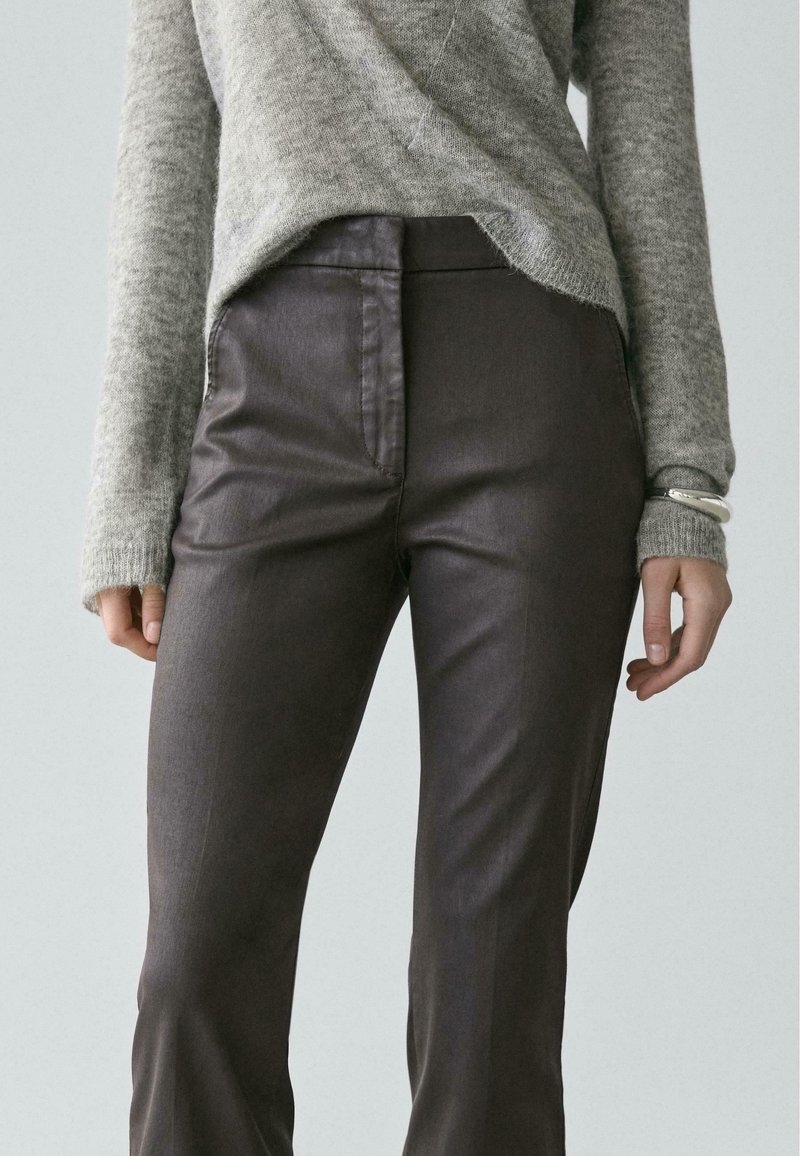 Person wearing dark brown pants and a light gray long-sleeve sweater, shown from mid-torso to upper legs, standing with hands relaxed.