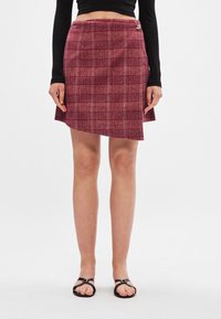 Sarkans svītrainais svārks ar asimetrisku apakšmalu, izgatavots no struktūras auduma, ar sānu poga akcentu. Apvienots ar melnām siksnu sandālēm.