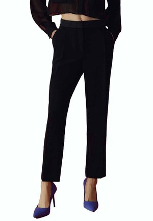 Pantaloni neri su misura con vestibilità slim, tasche frontali e texture liscia, abbinati a tacchi alti viola.