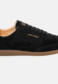 Schwarze Wildleder-Sneaker mit einer Sohle aus Gummi, flachen Schnürsenkeln und goldfarbener "HENRY STEVENS"-Markierung an der Seite. Klassisches Low-Top-Design.