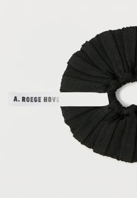 Fascia per capelli in tessuto nero con texture plissettata, con etichetta bianca con la scritta "A. ROEGE HOVE" stampata in grigio. Forma circolare.