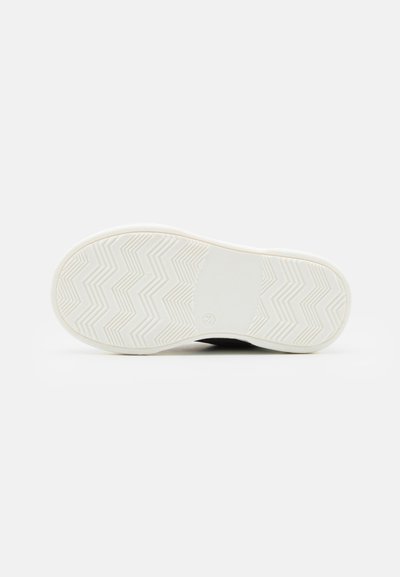 Suela de zapato negra con una parte inferior de goma blanca texturizada que presenta patrones en zigzag y una zona central lisa. El diseño es minimalista y funcional.