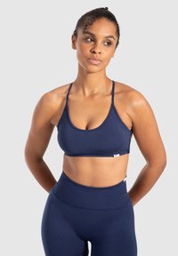 Sujeción deportiva azul marino con tirantes finos y un diseño simple. Fabricado con una tela suave y elástica, cuenta con una etiqueta de logo cerca del dobladillo.