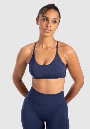 Sujeción deportiva azul marino con tirantes finos y un diseño simple. Fabricado con una tela suave y elástica, cuenta con una etiqueta de logo cerca del dobladillo.