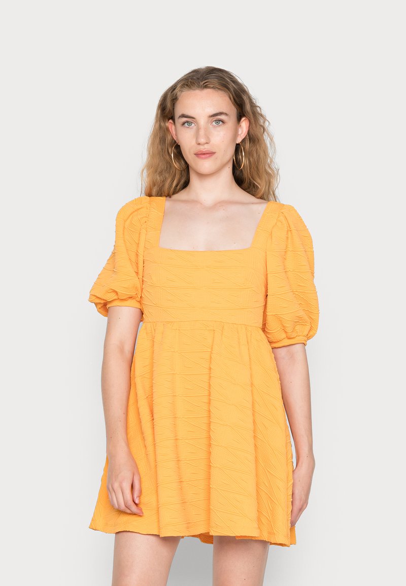 Vestido curto com mangas bufantes em tecido amarelo texturizado; decote quadrado e saia rodada. Apresenta um padrão subtil em todo o material.