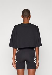 Černé zkrácené tričko volného střihu s krátkými rukávy, spojené s černými šortkami s bílými bočními proužky a detailním logem.