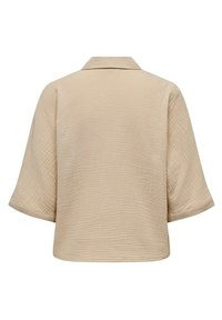 Blusa in cotone beige con finitura testurizzata, caratterizzata da un collo a camicia e maniche ampie. Il design è rilassato e squadrato.