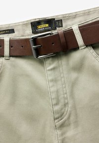 Jasno khaki spodnie z teksturowanej tkaniny, z brązowym skórzanym paskiem i metalową klamrą, gładkimi szwami oraz metką marki na pasku.