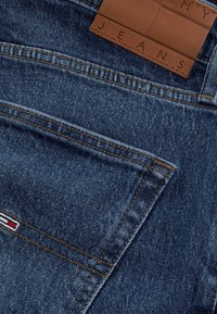 Kék farmernadrág varrott hátsó zsebbel, egy kis piros-fehér-kék zászló részlettel és egy barna bőr címkével, melyen az áll: "MY JEANS."