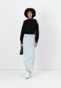 Črna bluza s spuščenimi rameni in dolgimi rokavi, v kombinaciji z lahko modro denimsko maksi krilo in belimi supergami, drži malo črno torbico.