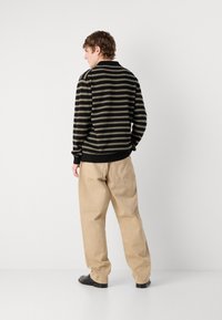 Pull rayé noir et beige avec col, porté avec un pantalon beige ample. L'ensemble présente une coupe décontractée et des poignets côtelés.