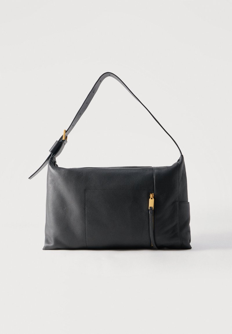 Μαύρη δερμάτινη τσάντα ώμου με ρυθμιζόμενο λουρί και χρυσή λεπτομέρεια φερμουάρ στην μπροστινή τσέπη, τοποθετημένη πάνω σε απλό φωτεινό φόντο.