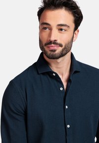 Donkerblauwe gemêleerde polo met kraag, voorzien van witte knopen. De stof lijkt lichtgewicht en ademend, geschikt voor casual wear.