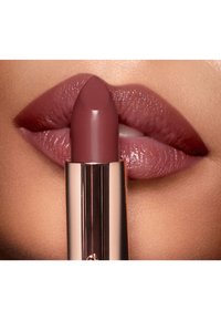 Lippenstift in einer rosaroten Nuance, der vor volleren, sanft strukturierten Lippen gehalten wird. Die Hülse hat eine elegante, metallisch goldene Verpackung.