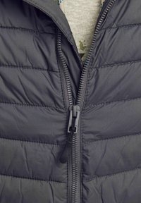 Grijze puffer vest met horizontale stiksels, een voorruitser en een gladde stofstructuur. Heldere voering zichtbaar binnenin bij de kraag.
