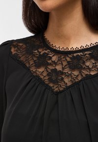 Blusa preta com um corpete rendado com padrões florais, decote redondo e tecido pregueado na parte inferior. Textura suave, design elegante.