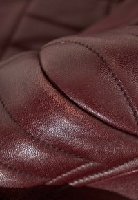 Gros plan sur un cuir cousu brun profond avec un grain visible et une texture de rembourrage lisse.
