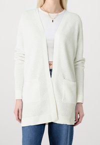 Cardigan léger en maille crème avec un motif texturé. Comprend un col en V, une ouverture devant, et deux poches avant. Poignets et ourlet côtelés.