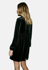 Abito in velluto nero con maniche lunghe, scollatura rotonda e vestibilità ampia, caratterizzato da una vita arricciata e un leggero lucido.