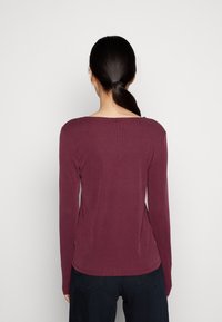 Bordeauxfarbener Langarmshirt mit geripptem Textur, weitem Ausschnitt und taillierter Passform. Schlichte Gestaltung ohne Verzierungen.