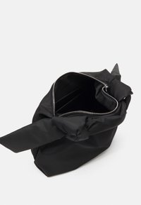 Borsa nera in nylon con cerniera superiore aperta, manico annodato, texture liscia, scomparti interni e dettagli con cerniera argentata.