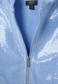 Hellblaues Zip-Jackett, das mit Pailletten bedeckt ist. Verfügt über einen silbernen Reißverschluss und ein Etikett, das die Größe für Kinder im Alter von 7-8 Jahren angibt.