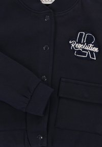 Marineblauwe sweatshirt met een ronde kraag, drukknoopjes en een gestructureerde "R Revolution" patch. Voorzien van ribgebreide manchetten en een voorzak.