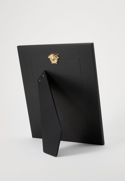 Czarne ramka na zdjęcia z teksturowanym wykończeniem, ozdobiona złotym głową lwa. Tył wyposażony w trójkątną podpórkę.