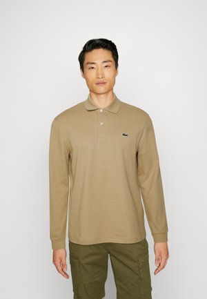 Langærmet polo i tan bomuld med krave og tre knapper, med et lille grønt logo på venstre bryst. Stylet med olivengrønne cargo shorts.