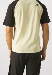 Cotton T-shirt med sorte raglanærmer; lys beige krop; har logo på ryggen. Casual design, afslappet pasform, korte ærmer.