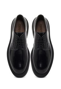 Chaussures en cuir noir avec une finition brillante, bout rond et sept œillets pour les lacets. Présentent une semelle en caoutchouc texturé pour une meilleure adhérence et durabilité.