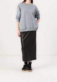 Grå oversize sweatshirt med sänkta axlar, kombinerad med en svart läder midi-kjol och svarta sneakers med gummisulor.