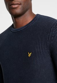 Navyblauer gerippter Strickpullover mit einem Rundhalsausschnitt und einem kleinen goldenen Adler-Logo auf der linken Brust. Strukturiert mit einem klassischen Schnitt.