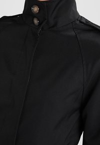 Černá saka s vysokým límcem, dvěma předními knoflíky, elegantním designem, hladkou texturou a mírnými detaily na ramenech.