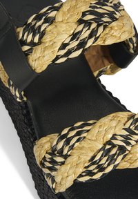 Black leather sandal featuring woven beige and black ropes across the straps, with a textured black platform sole.