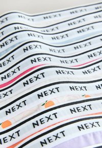 Rânduri de benzi textile pliate, cu cuvântul „NEXT” tipărit repetitiv în negru pe fundal alb, având margini de diferite culori.