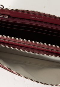 Cartera de cuero burdeos con cremalleras en tono plateado, que cuenta con múltiples ranuras para tarjetas y un interior suave y forrado. Logotipo visible en el interior.