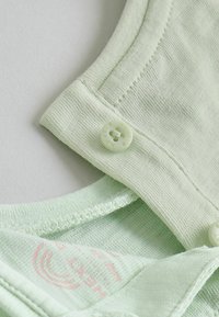 Gros plan sur un tissu vert clair avec des coutures cousues et de petits boutons ronds sur le col d’un vêtement.