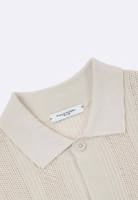 Polo shirt beige in maglia con un motivo testurizzato, chiusura con bottoni e colletto morbido. L'etichetta riporta "Paolo Pecora Milano."