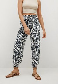 Pantalons de jogging à motifs bleu marine et blanc avec des poignets élastiques et une taille ajustable par cordon. Tissu léger, coupe décontractée, associés à des sandales plates.