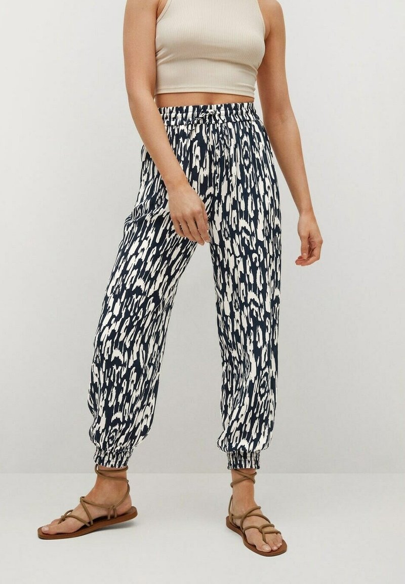 Pantalons de jogging à motifs bleu marine et blanc avec des poignets élastiques et une taille ajustable par cordon. Tissu léger, coupe décontractée, associés à des sandales plates.