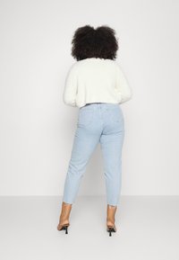 Pantalones vaqueros de talle alto en azul claro con piernas ligeramente ajustadas, dobladillos deshilachados, combinados con un suéter corto y esponjoso blanco y mules negros de tacón.