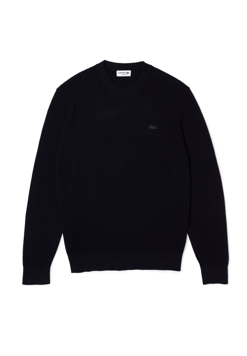 Marinblå stickad tröja, räfflad rund hals, långa ärmar, enfärgad, har en liten logotyp på bröstet, mjuk textur och åtsittande fåll och muddar.
