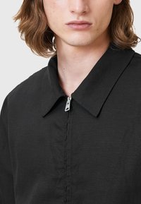 Svart zip-up skjorta med spetskrage, texturerad tyg och dold fram söm. Silverfärgad dragkedja på mitten fram.